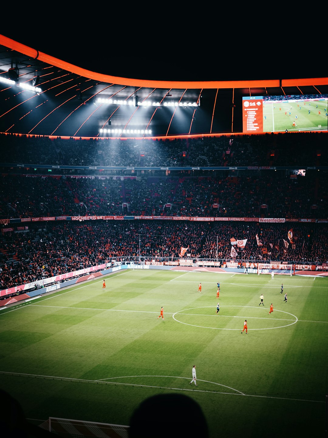 Football players compete on a brightly lit stadium field during a night game.