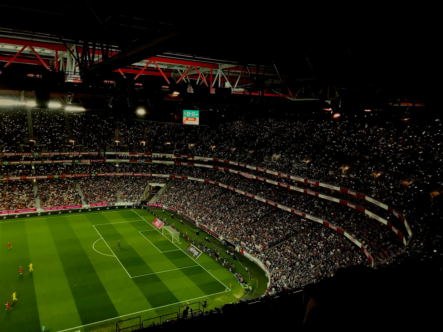 Football fans in a dark stadium hold up glowing cell phones.