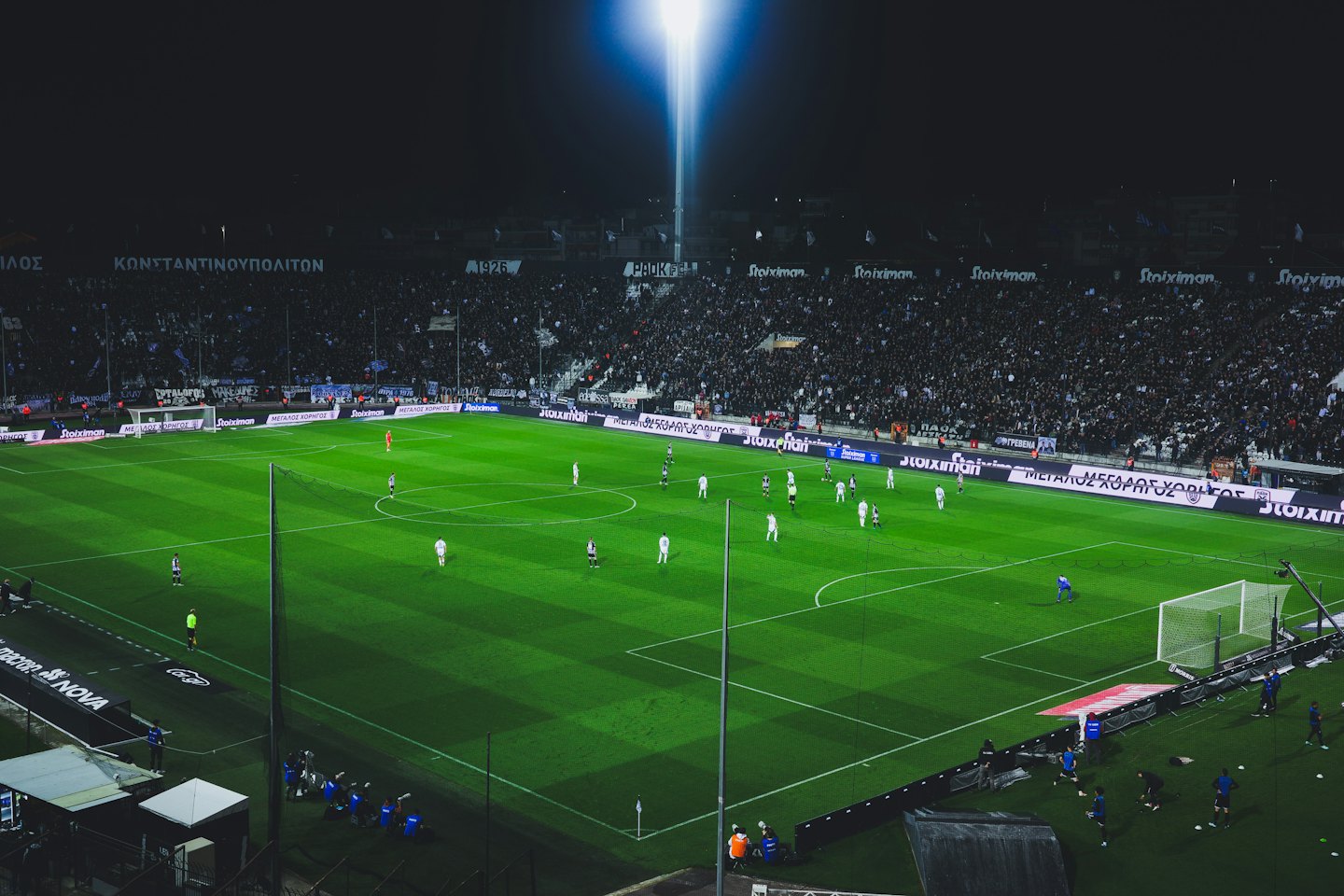 Football players compete on a bright green stadium field.